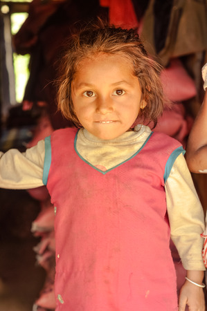 Beni, Nepal - circa May 2012: Small brown-haired girl in pink dress bites her lip in Beni, Nepal. Documentary editorial.のeditorial素材