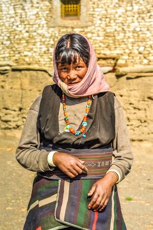 Dolpo, Nepal - circa June 2012: Black-haired woman in brown dress with pink headcloth wears colourful necklace made of beads in Dolpo, Nepal. Documentary editorial.のeditorial素材