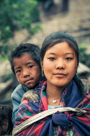 Dolpo, Nepal - circa May 2012: Young girl with long brown hair and earrings with her younger brother behind her with dirt on face and they look to photocamera in Dolpo, Nepal. Documentary editorial.のeditorial素材