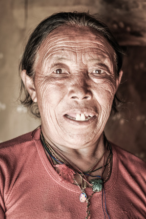 Dolpo, Nepal - circa May 2012: Old native woman with wrinkles and bright brown eyes wears necklaces in her house in Dolpo, Nepal. Documentary editorial.のeditorial素材