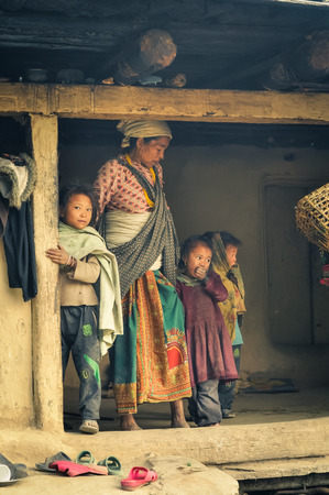 Dolpo, Nepal - circa May 2012: Native woman with white headcloth looks down and poses with her three young children in their wooden house in Dolpo, Nepal. Documentary editorial.のeditorial素材