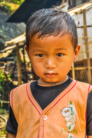 Kanchenjunga Trek, Nepal - circa April 2012: Small brown-eyed girl dressed in vest with dirt on her upper lip looks timidly to photocamera in Kanchenjunga Trek, Nepal. Documentary editorial.のeditorial素材