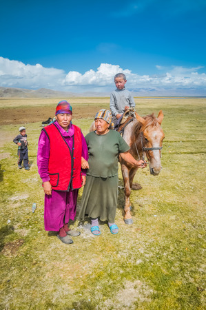 Son Kol, Kyrgyzstan - circa September 2011: Native women dressed in skirts and with headcloths pose in Son Kol, Kyrgyzstan. In the backgroud with young boy on horse. Documentary editorial.のeditorial素材
