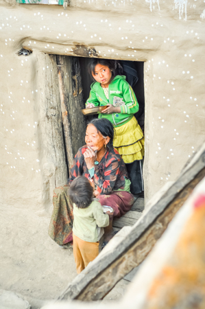 Dolpo, Nepal - circa May 2012: Old smiling woman sits on doorstep of her house with two young children who eat in Dolpo, Nepal. Documentary editorial.のeditorial素材
