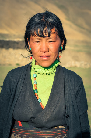 Dolpo, Nepal - circa June 2012: Young black-haired woman dressed in green shirt and grey sweatshirt wears blue and red earrings in Dolpo, Nepal. Documentary editorial.のeditorial素材