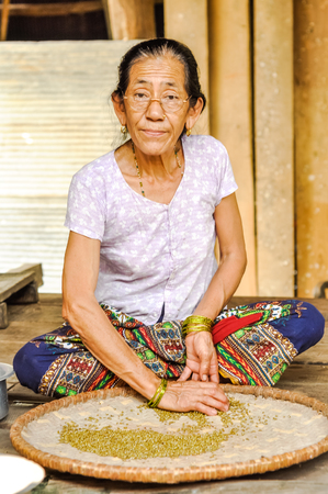 Damak, Nepal - circa May 2012: Native woman with glasses and yellow bracelets on her hands sits on ground in front of plate with grains in Damak, Nepal. Documentary editorial.のeditorial素材