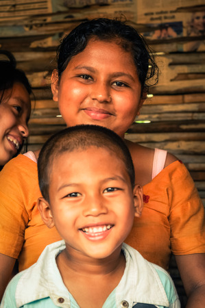 Damak, Nepal - circa May 2012: Young girl in orange t-shirt poses with younger boy in white t-shirt and they smile to photocamera at Nepali refugee camp in Damak, Nepal. Documentary editorial.のeditorial素材