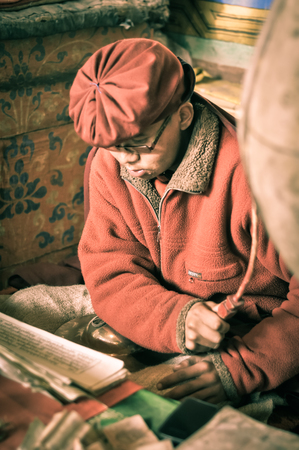 Hemis, Ladakh - circa November 2011: Young monk dressed in red clothes studies and reads documents at Tibetan Buddhist monastery in Hemis, Ladakh. Documentary editorial.のeditorial素材