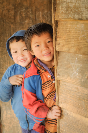 Dorjeling, Arunachal Pradesh - circa March 2012: Two young boys hide timidly behind wall and look to photocamera at school in Dorjeling, Arunachal Pradesh. Documentary editorial.のeditorial素材