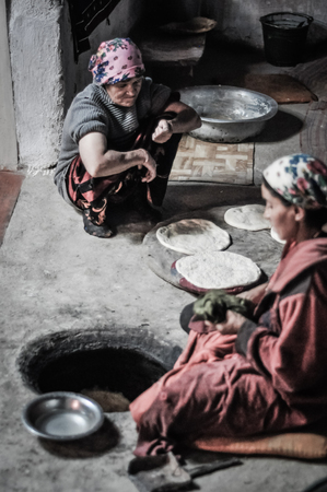 Wakhan valley, Tajikistan - circa October 2011: Women sit on ground during preparation of flat cakes over fire in Wakhan valley, Tajikistan. Documentary editorial.のeditorial素材