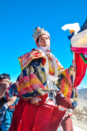 Thiksey, Ladakh - circa November 2011: Monk in traditional colourful costume and red flags in his hands dances during festival at Thiksey monastery, Ladakh. Documentary editorial.のeditorial素材