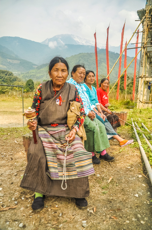 Tuting, Arunachal Pradesh - circa March 2012: Older native women sit on bench and look to photocamera in Tuting, Arunachal Pradesh. Documentary editorial.のeditorial素材