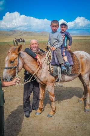 Son Kol, Kyrgyzstan - circa September 2011: Two small boys pose on horseback in Son Kol, Kyrgyzstan. Near them stand their father. Documentary editorial.のeditorial素材