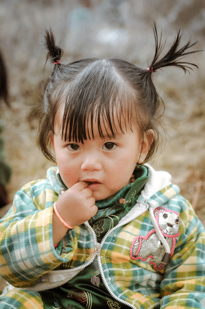 Dorjeling, Arunachal Pradesh - circa March 2012: Small girl with two ponytails has finger in her mouth in Dorjeling, Arunachal Pradesh. Documentary editorial.のeditorial素材