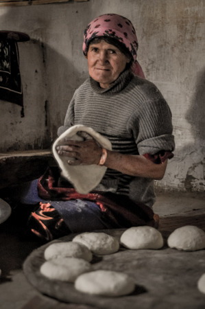 Wakhan valley, Tajikistan - circa October 2011: Older woman with pink headcloth sits on ground and kneads dough in Wakhan valley, Tajikistan. Documentary editorial.のeditorial素材