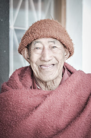 Tawang, Arunachal Pradesh - circa February 2012: Older man in red with orange cap on his head smiles and looks happily to photocamera in Tawang, Arunachal Pradesh. Documentary editorial.のeditorial素材
