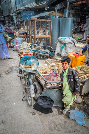 Kabul, Afghanistan - circa October 2011: Young native boy stands next to cages with animals at marketplace in Old town, old city part in Kabul. Documentary editorial.のeditorial素材