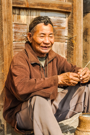 Ziro, Arunachal Pradesh - circa March 2012: Older man in brown shirt sits on ground and talks in Ziro, Arunachal Pradesh. Documentary editorial.のeditorial素材