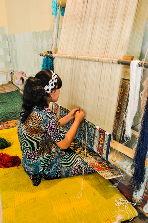 Margilan, Uzbekistan - circa July 2011: Woman weaves carpet in Yodgorlik Silk Factory in Margilan. Documentary editorial.のeditorial素材
