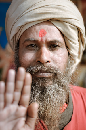 Ganga Sagar, West Bengal - circa January 2012: Man with long grey beard and red dot on forehead wears turban and holds his hand towards photocamera in Ganga Sagar, West Bengal. Documentary editorial.のeditorial素材