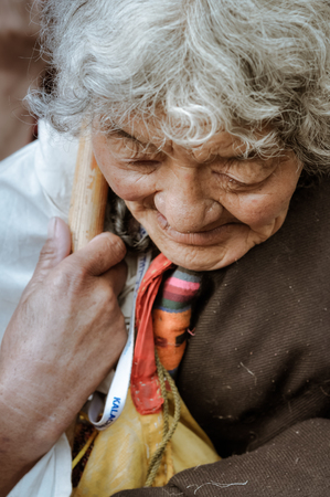 Bohdgaya, Bihar - circa January 2012: Old woman with grey hair holds wooden stick and looks down in Bohdgaya, Bihar. Documentary editorial.のeditorial素材