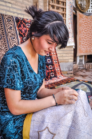 Khiva, Uzbekistan - circa July 2011: Young woman dressed in blue embroiders table clothing in Khiva, Uzbekistan. Documentary editorial.のeditorial素材