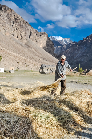 Khorog, Tajikistan - circa September 2011: Man with cap holds hayfork and works with hay in Khorog, Tajikistan. Documentary editorial.のeditorial素材