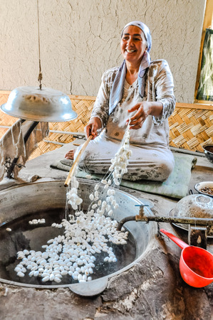 Margilan, Uzbekistan - circa July 2011: Smiling woman sits on ground and adds silk worm cocoons to vat with water in silk factory in Margilan. Documentary editorial.のeditorial素材