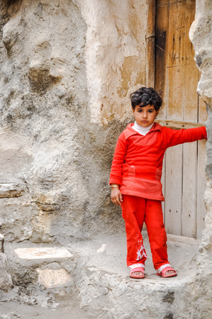 Kandovan, Iran - circa June 2011: Small girl in red clothes stands in front of her rock house in rocky village of Kandovan in Iran. Documentary editorial.のeditorial素材