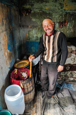 Son Kol, Kyrgyzstan - circa September 2011: Smiling native man stirs content of wooden barrel in Son Kol, Kyrgyzstan. Documentary editorial.のeditorial素材