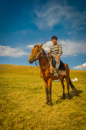 Son Kol, Kyrgyzstan - circa September 2011: Young native man poses on his brown horse in beautiful countryside of Son Kol, Kyrgyzstan. Documentary editorial.のeditorial素材