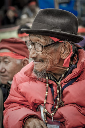 Bohdgaya, Bihar - circa January 2012: Old man with wrinkled face wears black hat on his head and red jacket and listens with humble smile in Bohdgaya, Bihar. Documentary editorial.のeditorial素材