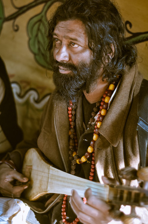 Shantiniketan, West Bengal - circa January 2012: Man with longer black hair and beard plays musical instrument at Baul music festival near Shantiniketan, West Bengal. Documentary editorial.のeditorial素材