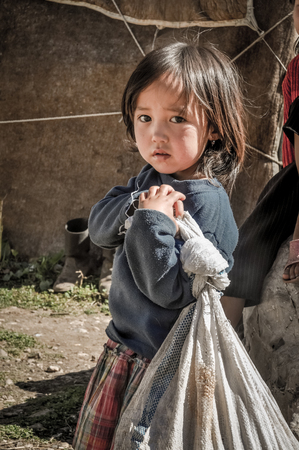 Arslanbob, Kyrgyzstan - circa July 2011: Young native girl with sad face holds pack and poses in Arslanbob, Kyrgyzstan. Documentary editorial.のeditorial素材