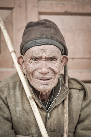 Ziro, Arunachal Pradesh - circa March 2012: Old man with tanned face and cap on his head holds wooden stick in Ziro, Arunachal Pradesh. Documentary editorial.のeditorial素材