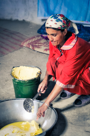 Wakhan valley, Tajikistan - circa October 2011: Woman in red clothes kneels and adds butter to large pot in Wakhan valley, Tajikistan. Documentary editorial.のeditorial素材