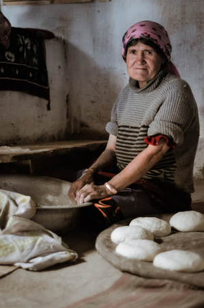Wakhan valley, Tajikistan - circa October 2011: Older woman with pink headcloth sits on ground during preparation of bread in Wakhan valley, Tajikistan. Documentary editorial.のeditorial素材