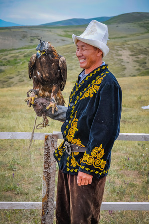 Karakol, Kyrgyzstan - circa July 2011: Native man dressed in traditional folk costume with Golden eagle on his arm at Karakol festival in Kyrgyzstan. Documentary editorial.のeditorial素材
