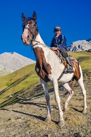 Arslanbob, Kyrgyzstan - circa July 2011: Native boy sits on horse in beautiful mountainous countryside of Arslanbob, Kyrgyzstan. Documentary editorial.のeditorial素材