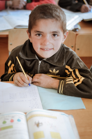 Khorog, Tajikistan - circa September 2011: Small boy smiles during writing at school in Khorog, Tajikistan. Documentary editorial.のeditorial素材