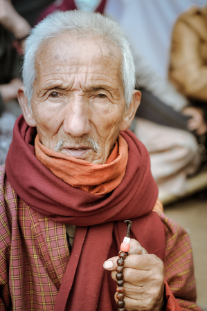Bohdgaya, Bihar - circa January 2012: Old man with red and orange scarf holds rosary in his hand in Bohdgaya, Bihar. Documentary editorial.のeditorial素材