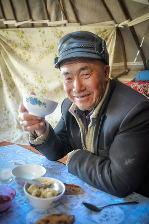 Son Kol, Kyrgyzstan - circa September 2011: Older man with leather cap sits at table during drinking of tea in Son Kol, Kyrgyzstan. Documentary editorial.のeditorial素材