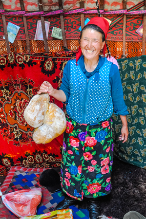 Ala Archa, Kyrgyzstan - circa September 2011: Native woman with red hat and colourful clothes in her tent in Ala Archa, Kyrgyzstan. She holds traditional food in her hand. Documentary editorial.のeditorial素材