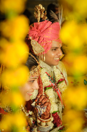 Bikaner, Rajasthan - circa December 2011: Smilimg wedding couple sits behind yellow decorations during wedding in Bikaner, Rajasthan. Documentary editorial.のeditorial素材