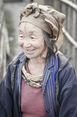 Ziro, Arunachal Pradesh - circa March 2012: Old smiling woman in blue jacket and with brown headcloth poses in Ziro, Arunachal Pradesh. Documentary editorial.のeditorial素材