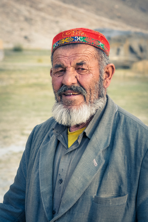 Khorog, Tajikistan - circa September 2011: Old man with tanned and wrinkled face in Khorog, Tajikistan. He wears grey suit and colourful cap. Documentary editorial.のeditorial素材
