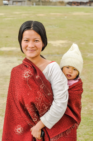 Ziro, Arunachal Pradesh - circa March 2012: Beautiful young woman carries her daughter on her back in Ziro, Arunachal Pradesh. Documentary editorial.のeditorial素材