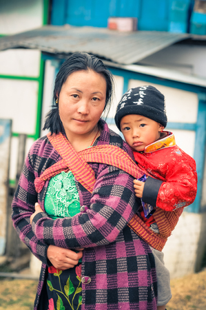 Khinmey Gompa and Ugyenling Temple, Arunachal Pradesh - circa February 2012: Woman with black hair carries her young son on her back in Khinmey Gompa, Arunachal Pradesh. Documentary editorial.のeditorial素材
