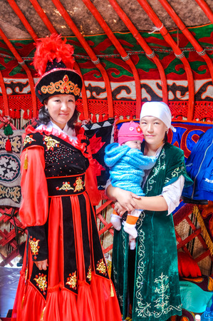 Karakol, Kyrgyzstan - circa August 2011: Two native women and child pose during Independence day in Karakol, Kyrgyzstan. Tall woman is dresseed in red and black folk costume. Documentary editorial.のeditorial素材