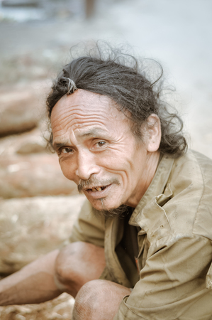 Ziro, Arunachal Pradesh - circa March 2012: Native man with long hair kneels and looks up to photocamera in Ziro, Arunachal Pradesh. Documentary editorial.のeditorial素材